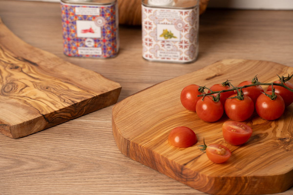 Oval olivewood charcuterie boards with natural grain patterns, one with rope handle, displayed with fresh tomatoes.