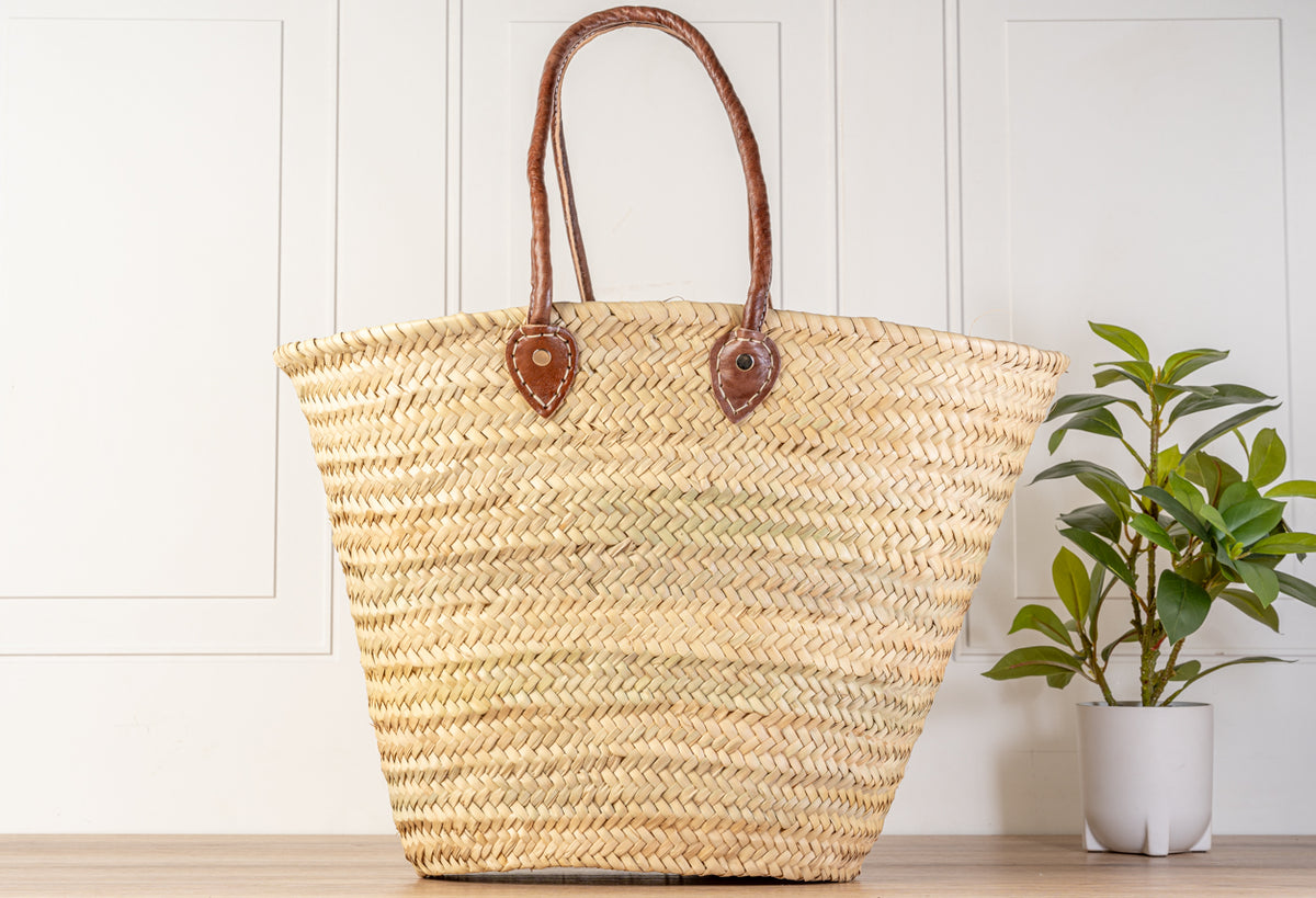 Woven straw basket with brown leather handles and herringbone pattern weave.