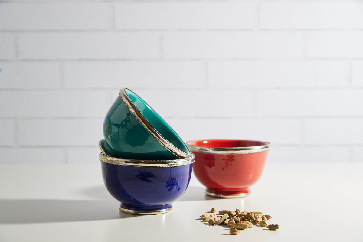 Three glazed bowls in teal, navy, and red with metallic trim around the rims.