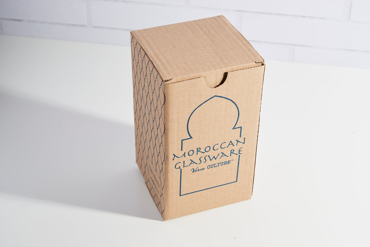 Cardboard shipping box with "Moroccan Glassware" printed logo and decorative cone jug illustration on tan kraft paper.
