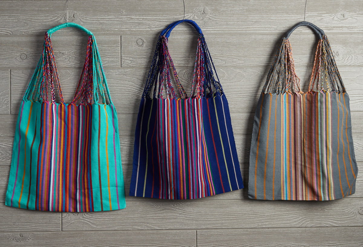 Three woven market hammock bags with vertical stripes in turquoise-red, navy-red, and gray-orange colorways displayed flat.