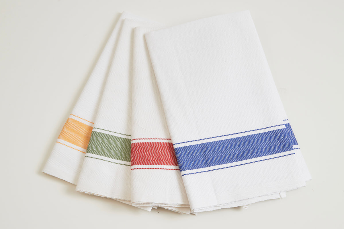 Four cream kitchen towels with herringbone weave and colored stripe trim in orange, green, red, and blue.