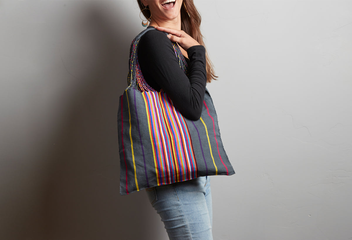 Woven shoulder bag with multicolored vertical stripes in red, yellow, blue, and green on dark background, worn on model's sho