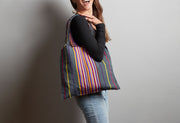 Woven shoulder bag with multicolored vertical stripes in red, yellow, blue, and green on dark background, worn on model's sho