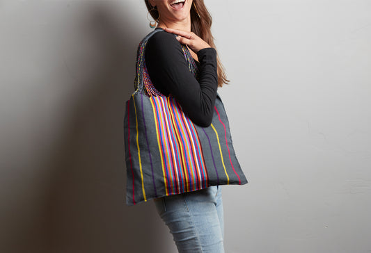 Woven shoulder bag with multicolored vertical stripes in red, yellow, blue, and green on dark background, worn on model's sho