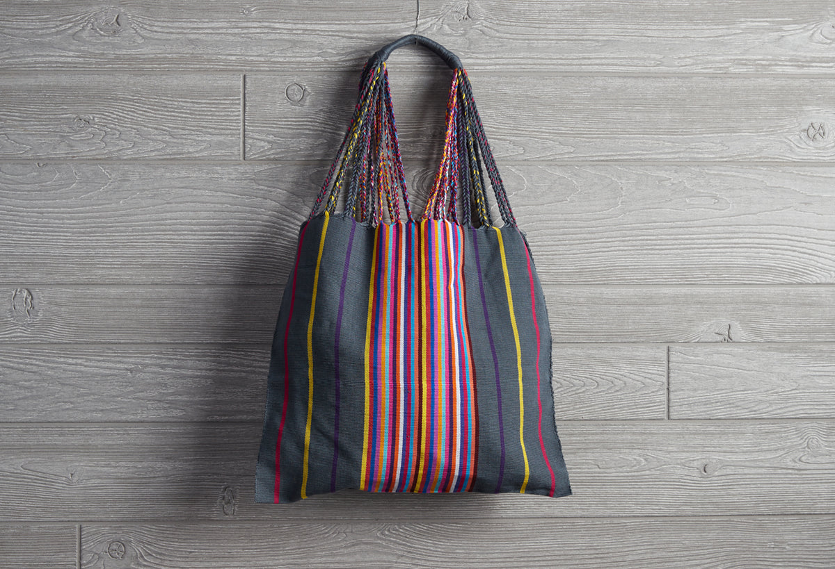 Woven market bag with multicolored vertical stripes in navy, red, yellow, and blue, featuring braided shoulder handles.