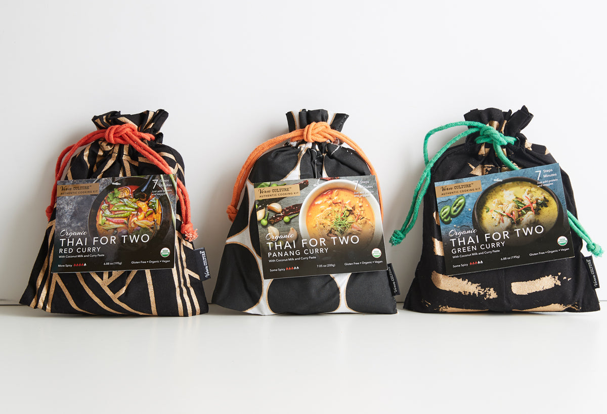 Three black drawstring pouches with red, orange, and green cords containing Thai curry products labeled red curry, panang cur