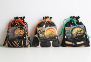 Three black drawstring pouches with red, orange, and green cords containing Thai curry products labeled red curry, panang cur