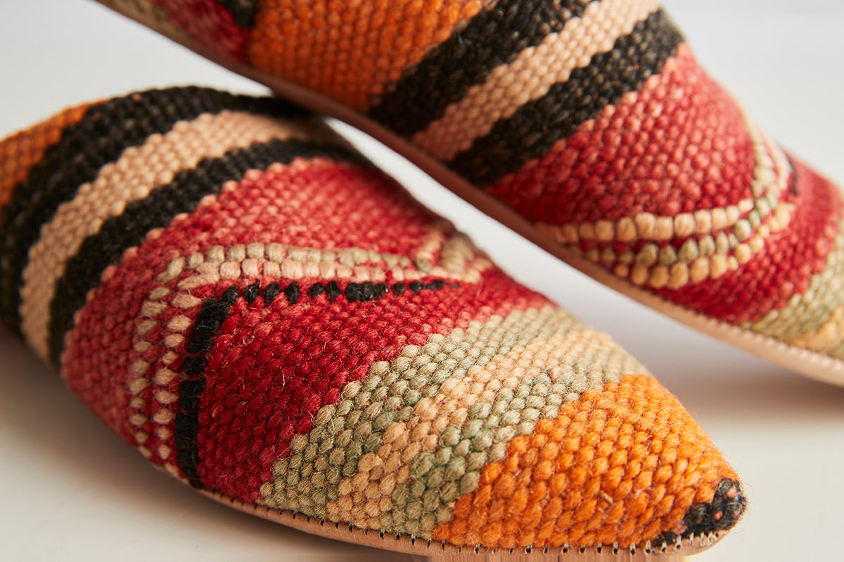 Pair of woven slippers with red, orange, black, and tan striped kilim pattern and pointed toes.