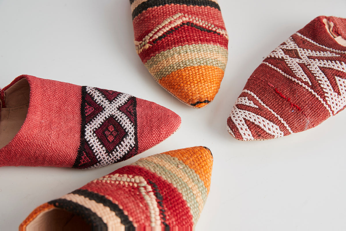 Pair of woven slippers with geometric patterns in red, orange, cream, and black kilim design.