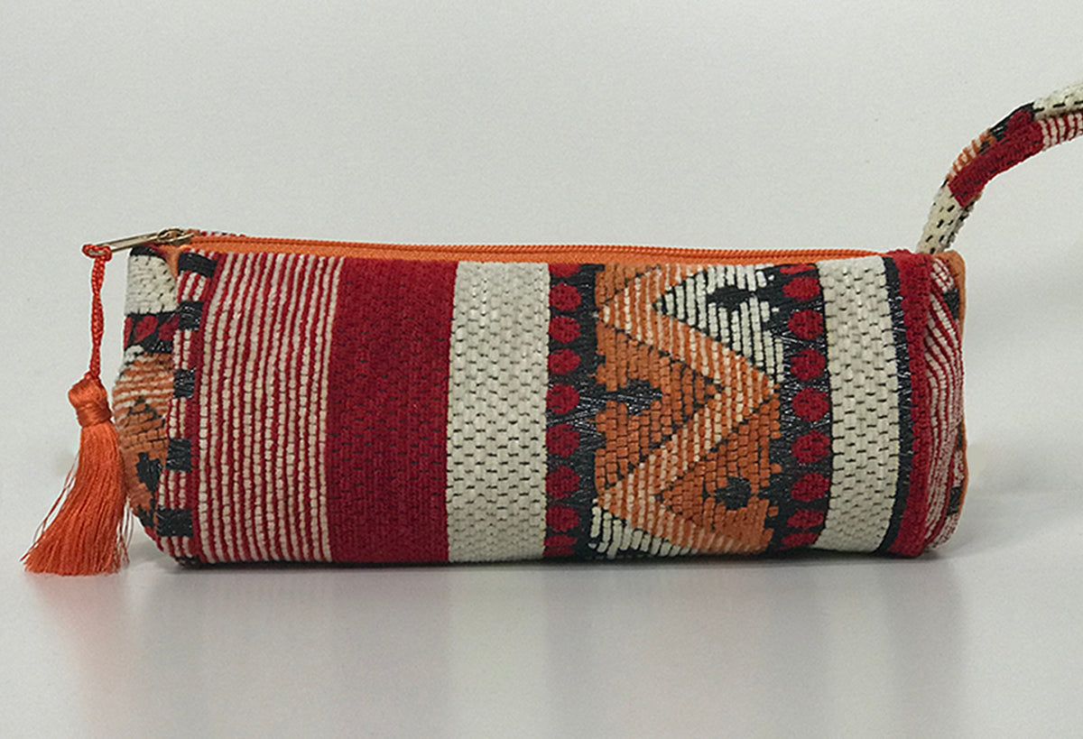 Barrel-shaped cosmetic bag with woven geometric pattern in burgundy, orange, cream, and black with tassel closure.