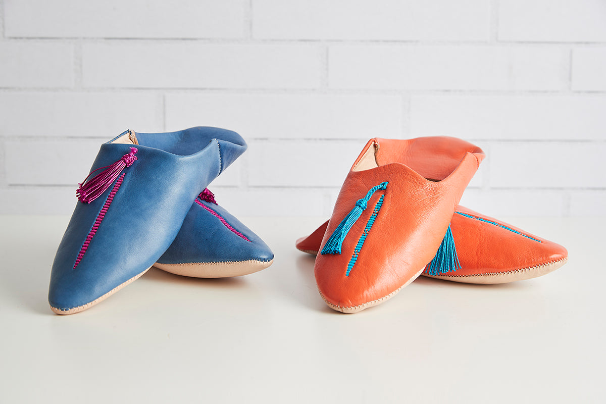 Pair of pointed-toe leather slippers in blue and coral with decorative tassels and contrast stitching.