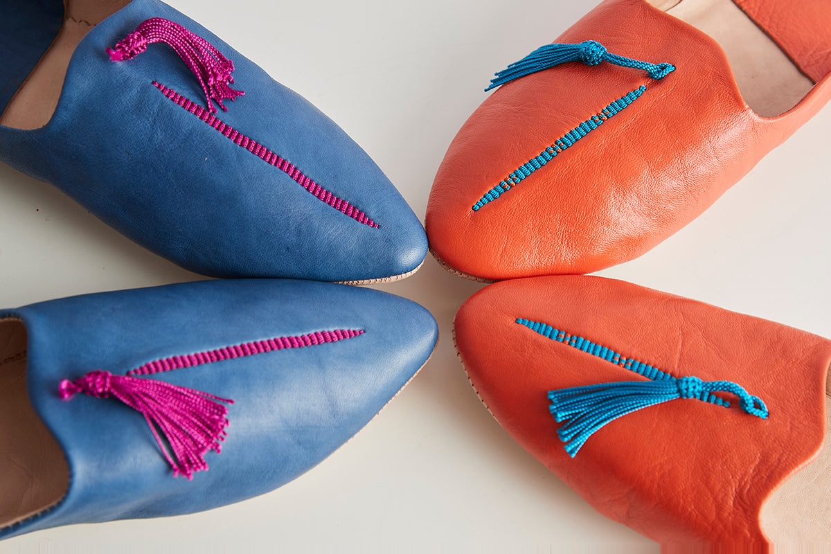 Two pairs of leather slippers in blue and orange with decorative beaded straps and tassels.
