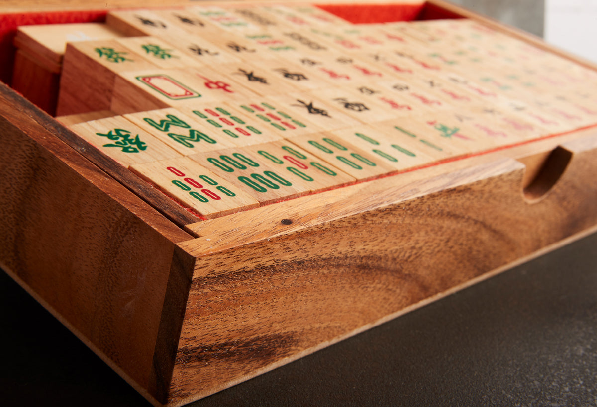Wooden Mahjong set with engraved tiles in green and red characters arranged on playing surface with storage compartments.