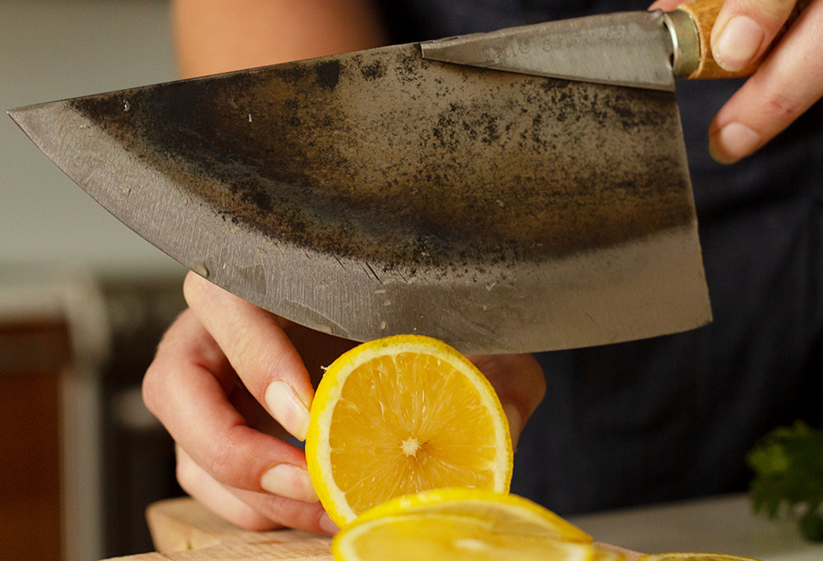 Curved Thai chef's knife with wooden handle held above sliced lemon.
