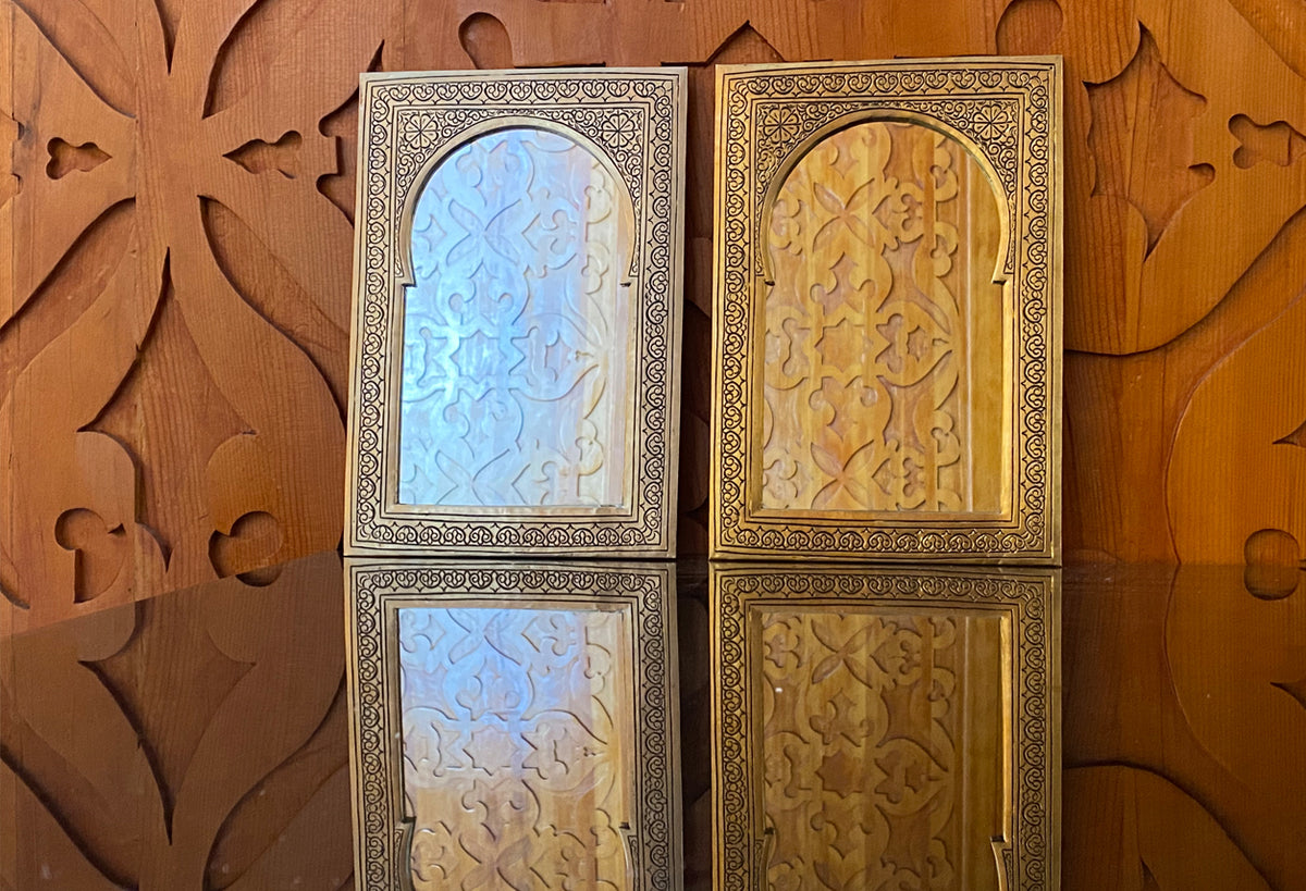 Two rectangular mirrors with ornate metal frames and geometric carved panels, one with blue-tinted glass and one with gold-to