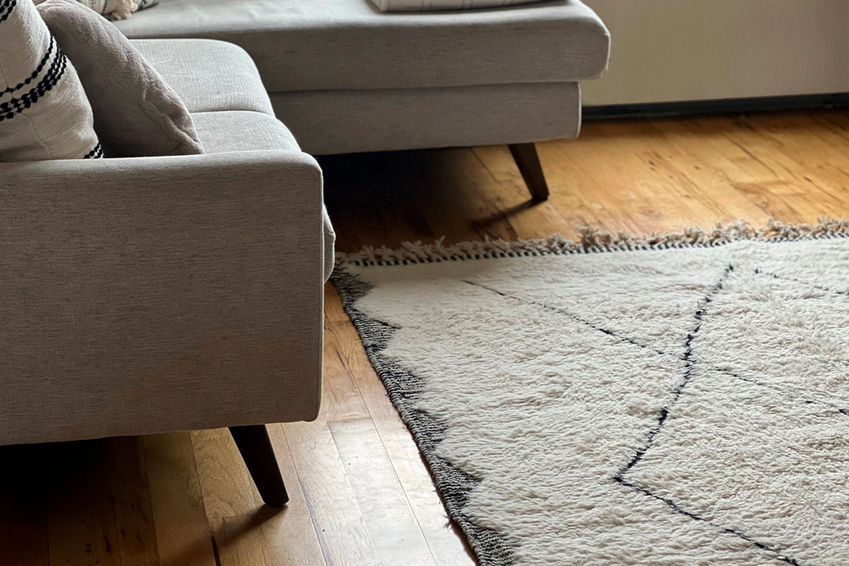 Cream and charcoal geometric patterned wool rug placed under a gray sofa on wooden flooring.