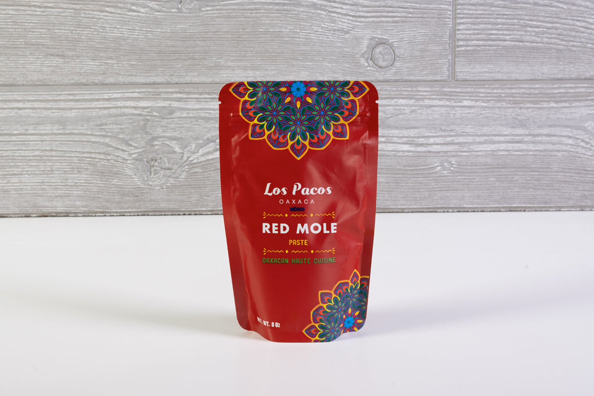 Red pouch of Los Pacos Red Mole Paste from Oaxaca with colorful floral design on wooden background.