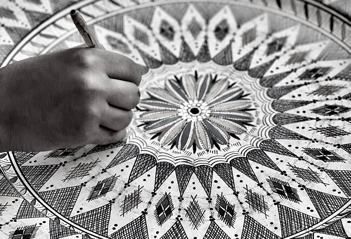 Child's hand resting on white ceramic platter with black geometric Moroccan patterns.