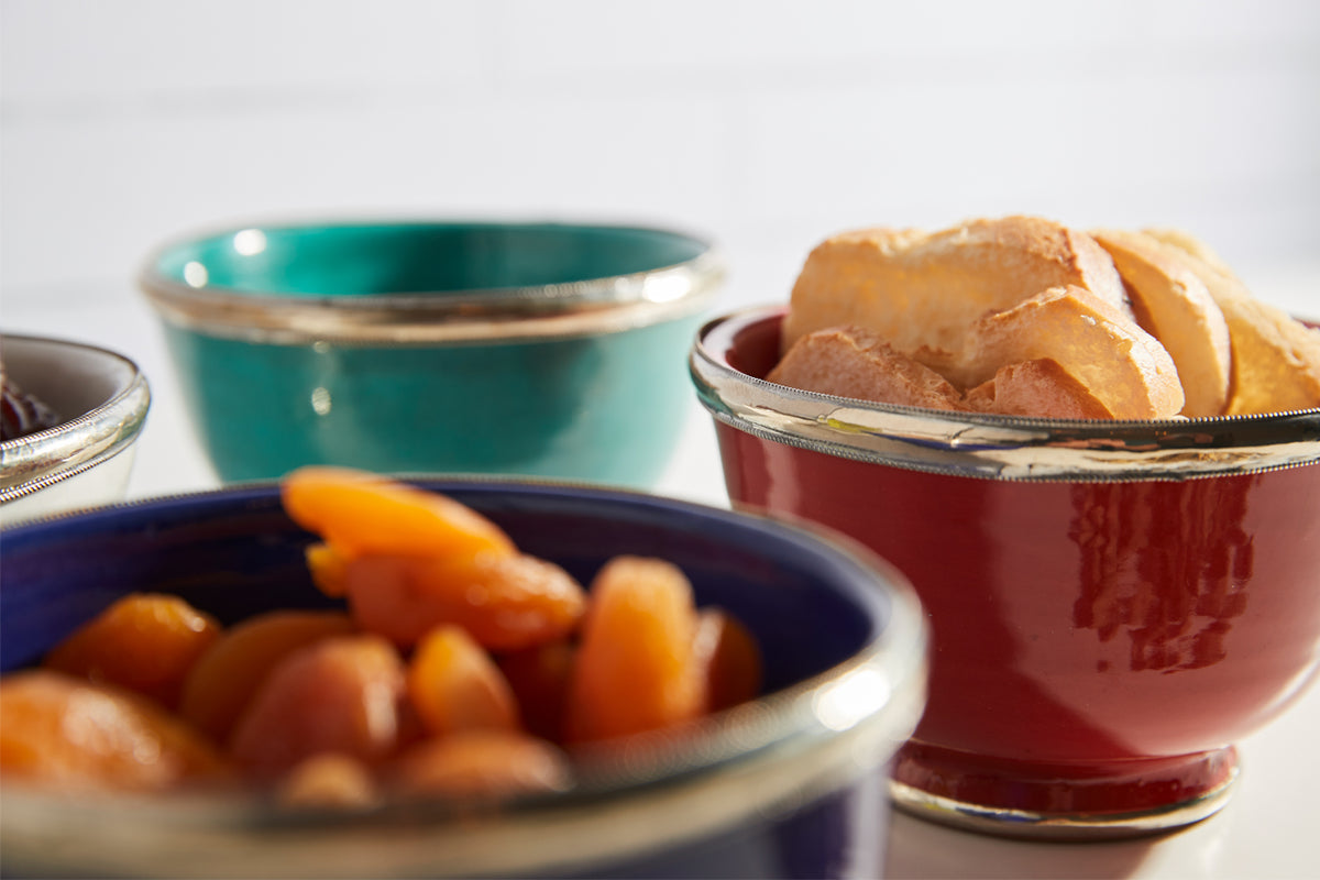 Three glazed ceramic bowls in turquoise, red, and blue with metallic trim, containing food items.