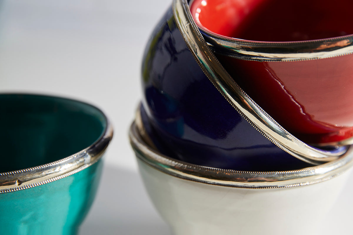 Three glazed bowls in turquoise, navy, and cream with decorative silver-tone metal trim around the rims.