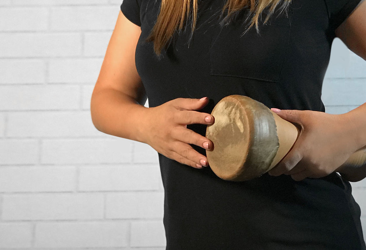 Person holding small round drum with natural leather head and woven fabric body.