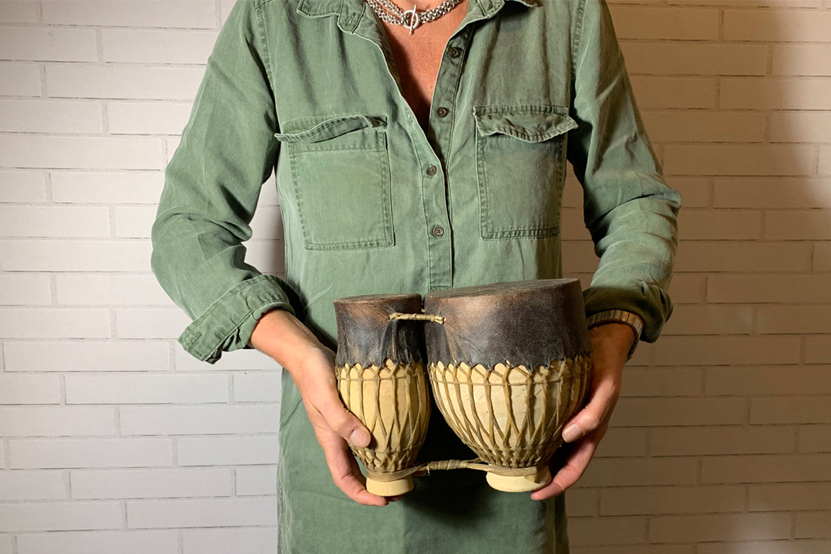 Moroccan tam-tam double drum with metal top and woven natural fiber body held by person in green shirt.