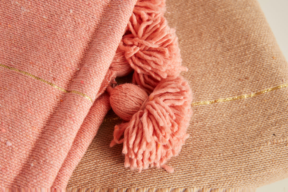 Pink and beige blankets with coral tassels and gold trim detail.