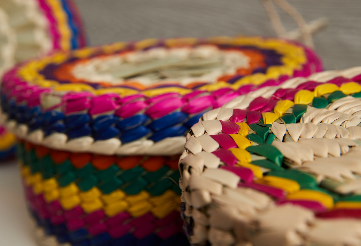 Woven palm basket with multicolored striped pattern in pink, yellow, blue, green, and natural tan.