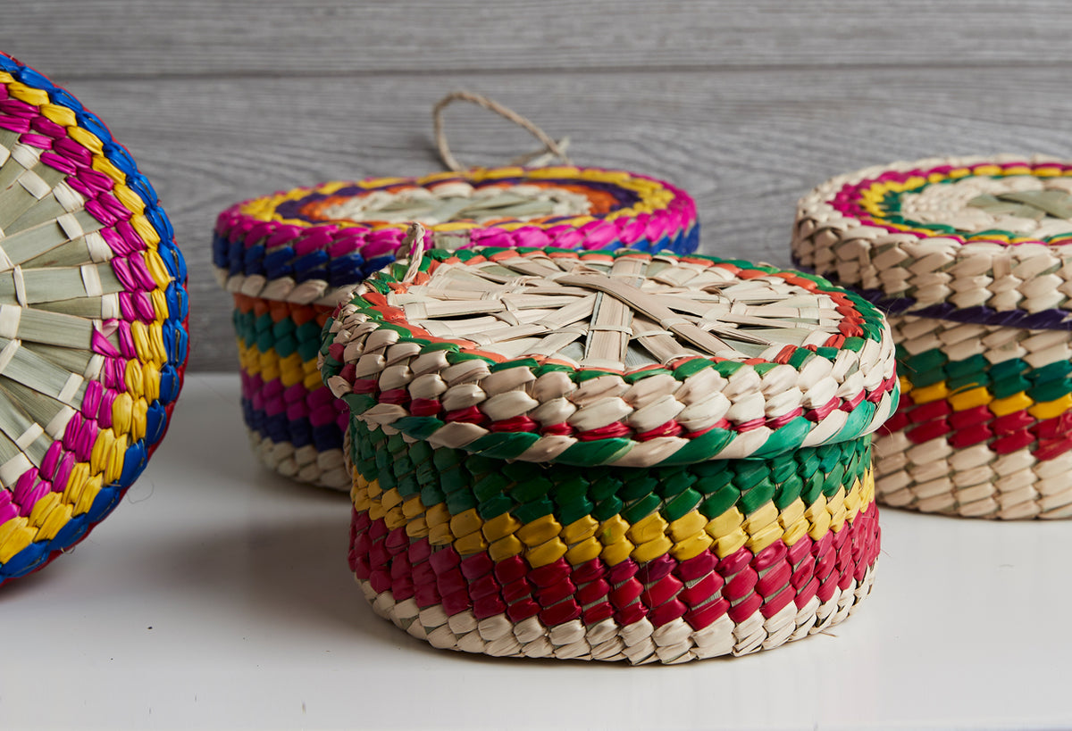 Three woven palm baskets with colorful striped patterns in red, yellow, green, blue and pink, each with a rope handle.