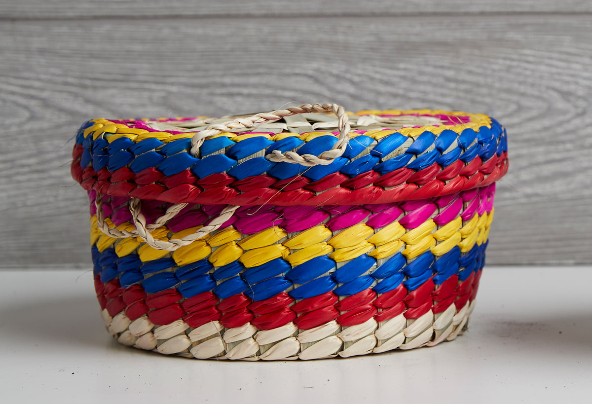 Woven palm basket with blue, red, yellow, magenta, and natural fiber stripes and twisted handles.