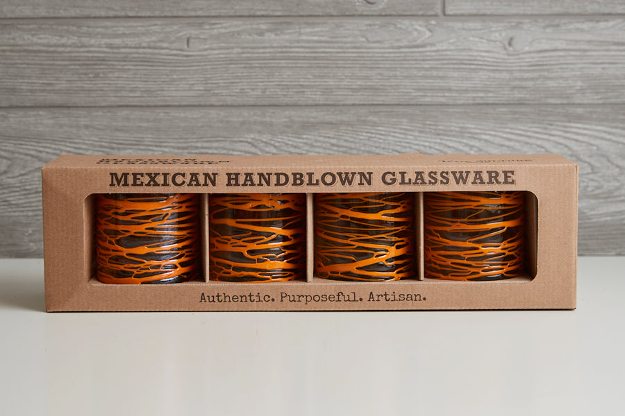 Four handblown glasses with orange and black striped pattern in cardboard packaging box.