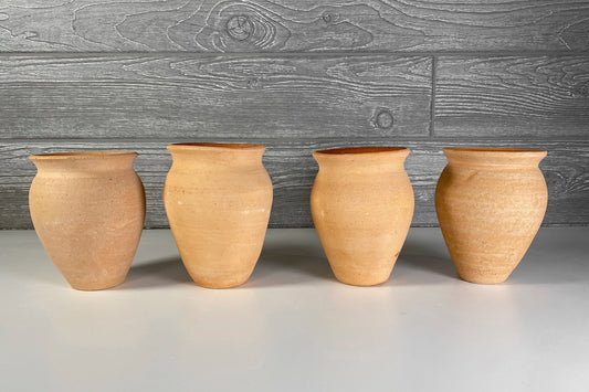 Four terracotta clay cups with wide mouths and rounded bodies arranged in a row.