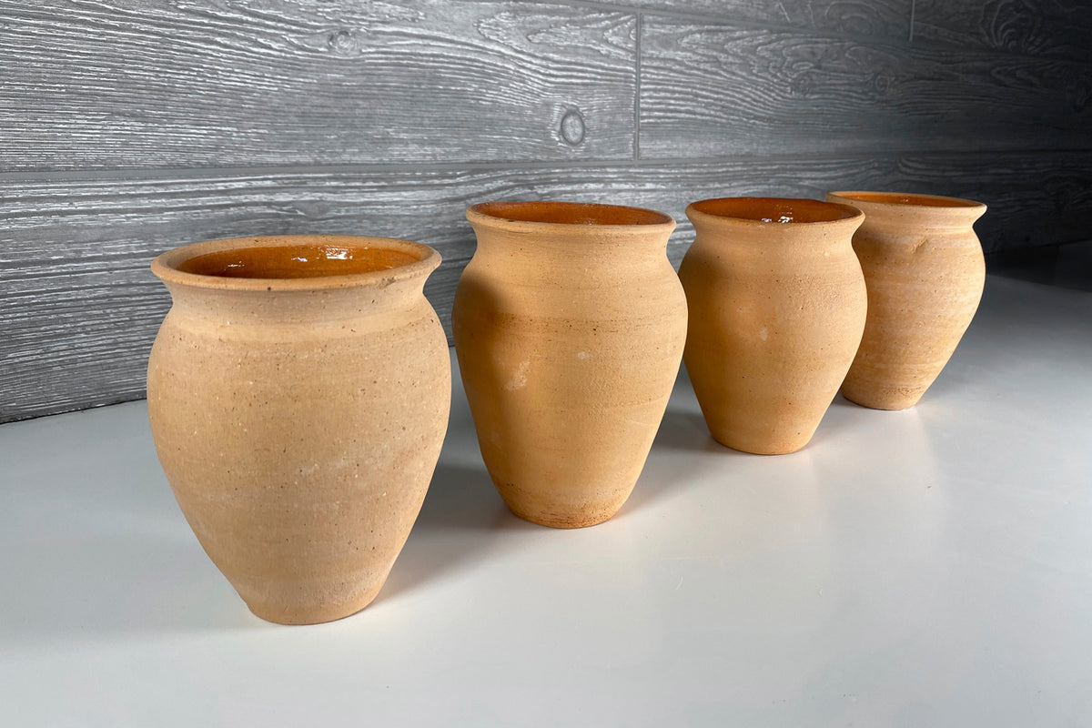 Four terracotta clay cups with rounded bodies and brown glazed interiors arranged in a row.