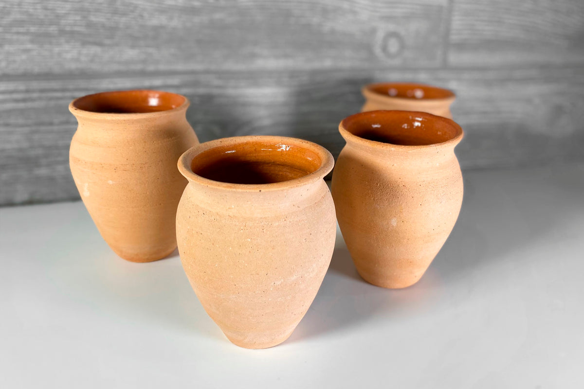 Four terracotta clay cups with wide mouths and glazed interiors in brown tones.