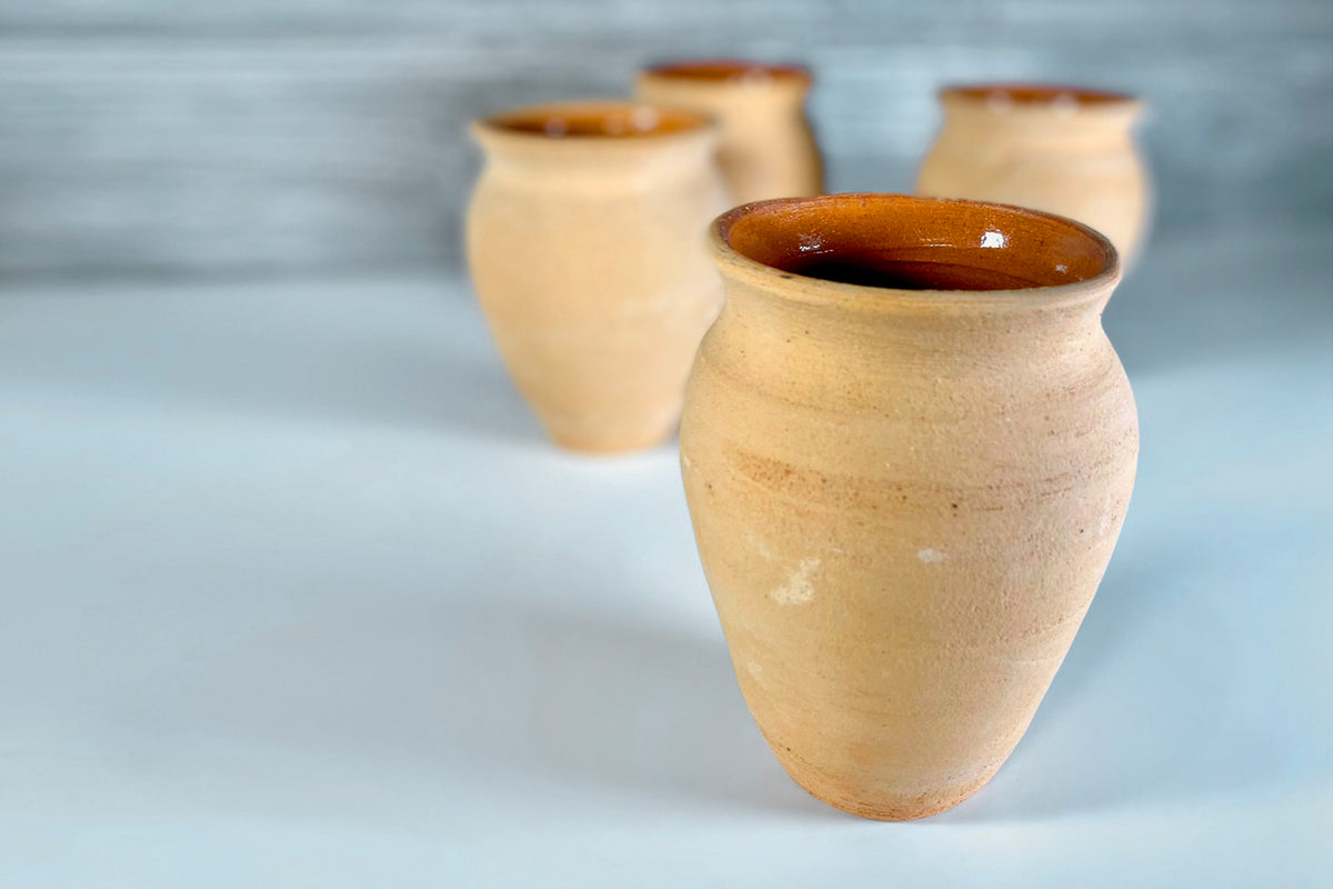 Four cream-colored clay cups with brown glazed rims and rounded bulbous bodies.