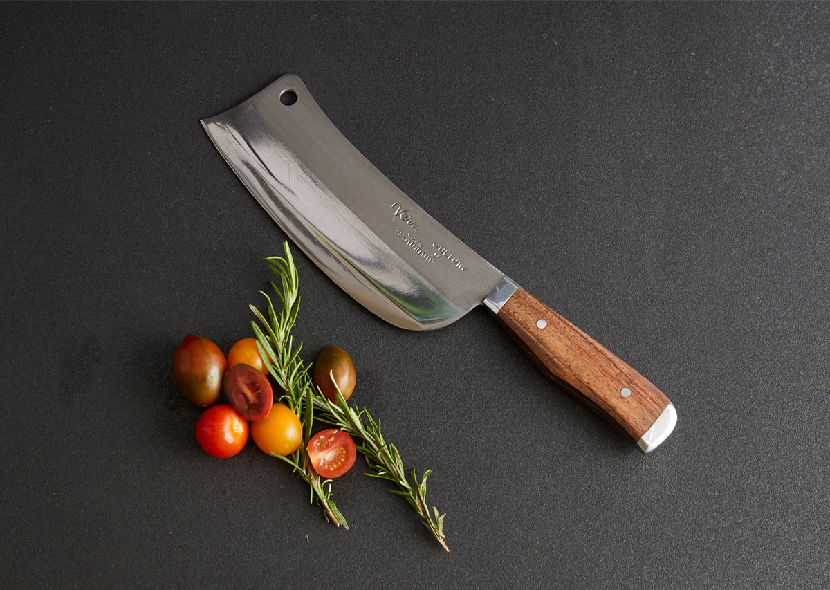Thai chef's knife with wide rectangular blade, wooden handle, and hole at top, displayed with fresh tomatoes and rosemary spr