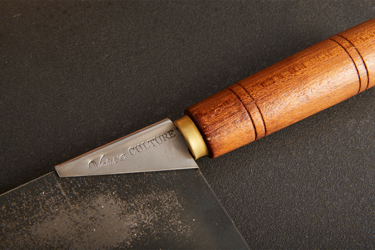 Curved cleaver blade with wooden handle and brass collar, engraved with "Verse Culture" text on gray background.