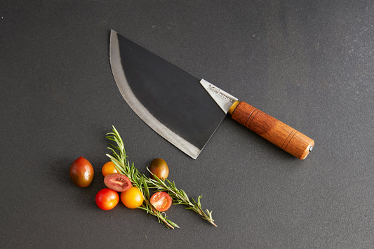 Curved chef's knife with wooden handle displayed above fresh tomatoes and rosemary sprigs on gray surface.