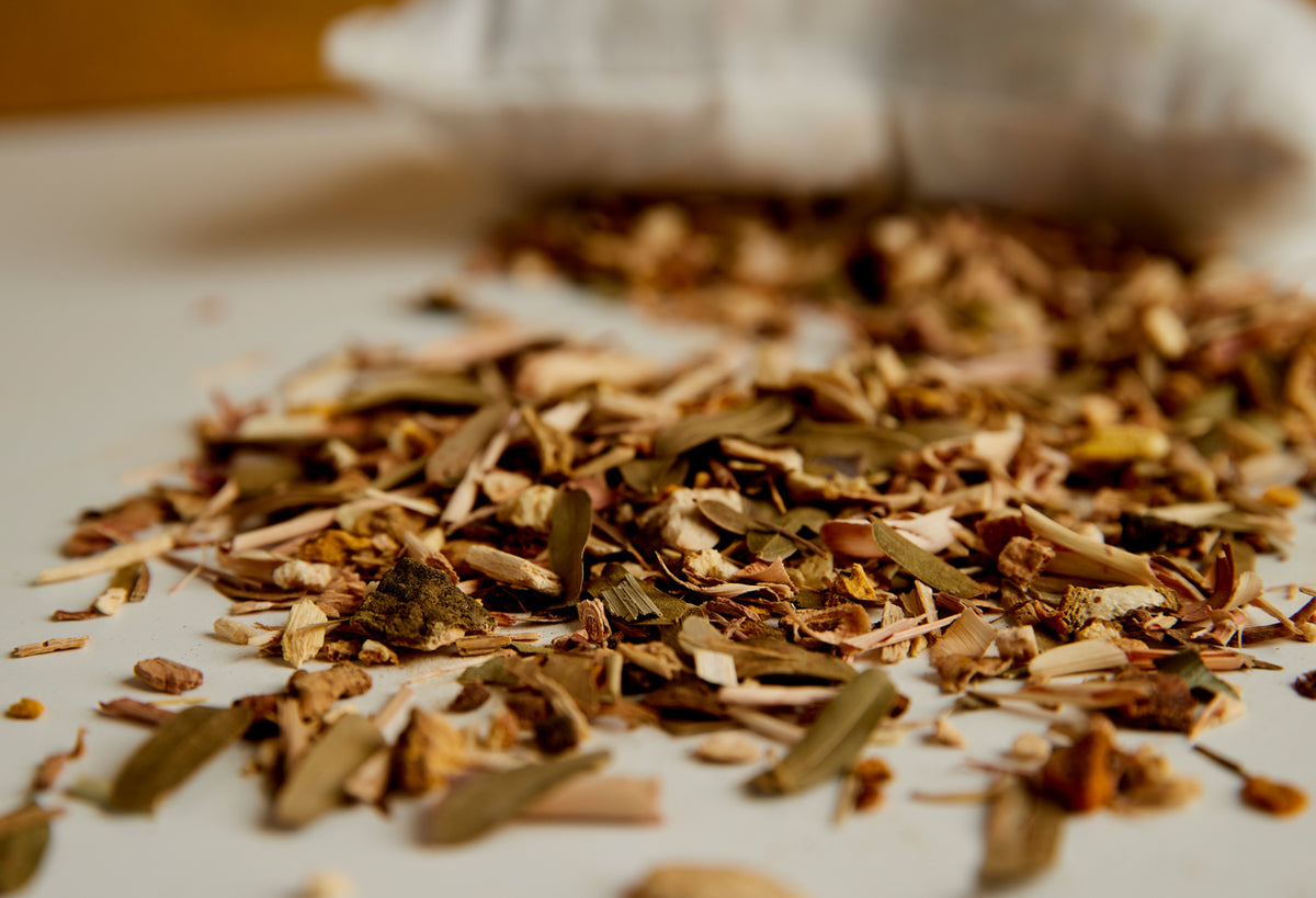 Dried herbal blend with bark, leaves, and plant fragments scattered on white surface.