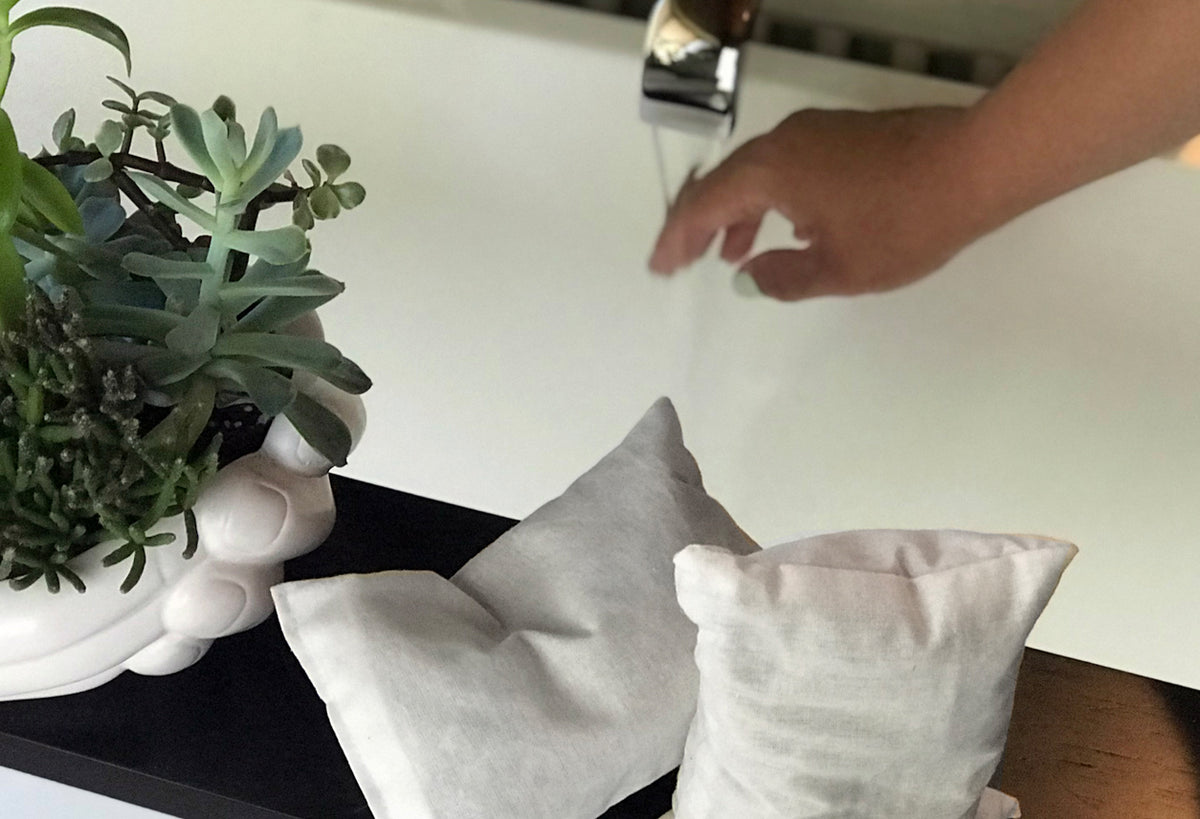 White muslin sachets filled with herbal bath soak next to potted succulent plant on bathroom counter.