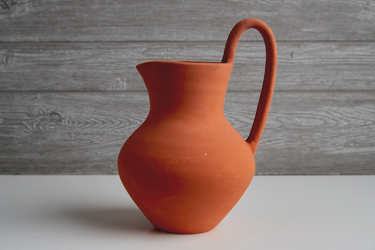 Red-orange ceramic jug with curved handle and tapered spout for pouring.