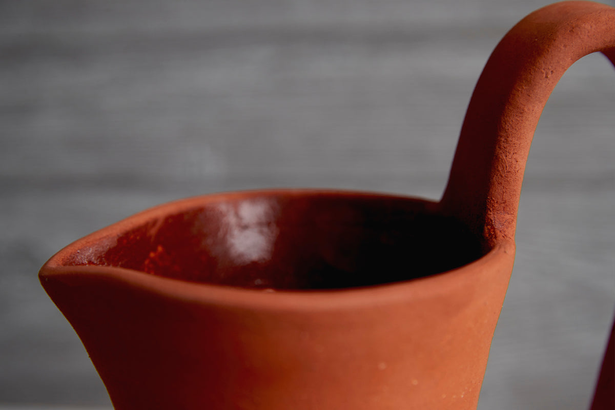Terracotta jug with curved handle and pouring spout, interior glazed in dark color.