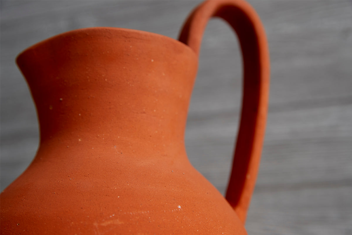 Rust-red ceramic jug with curved body, tapered neck, and arched handle.