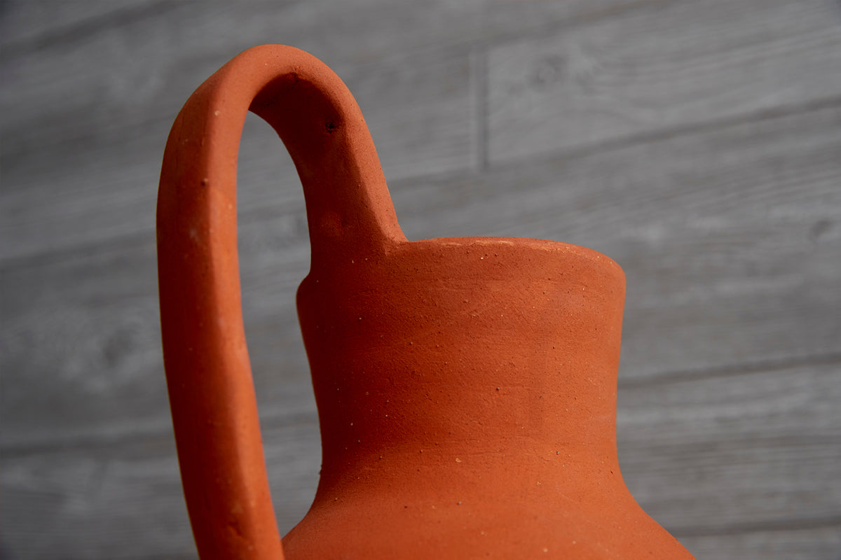 Terracotta jug with curved handle and wide spout, viewed from above against wooden background.