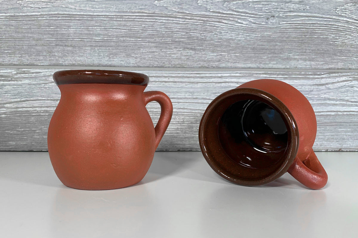Two terracotta mugs with dark brown interiors and handles, displayed from front and side angles.