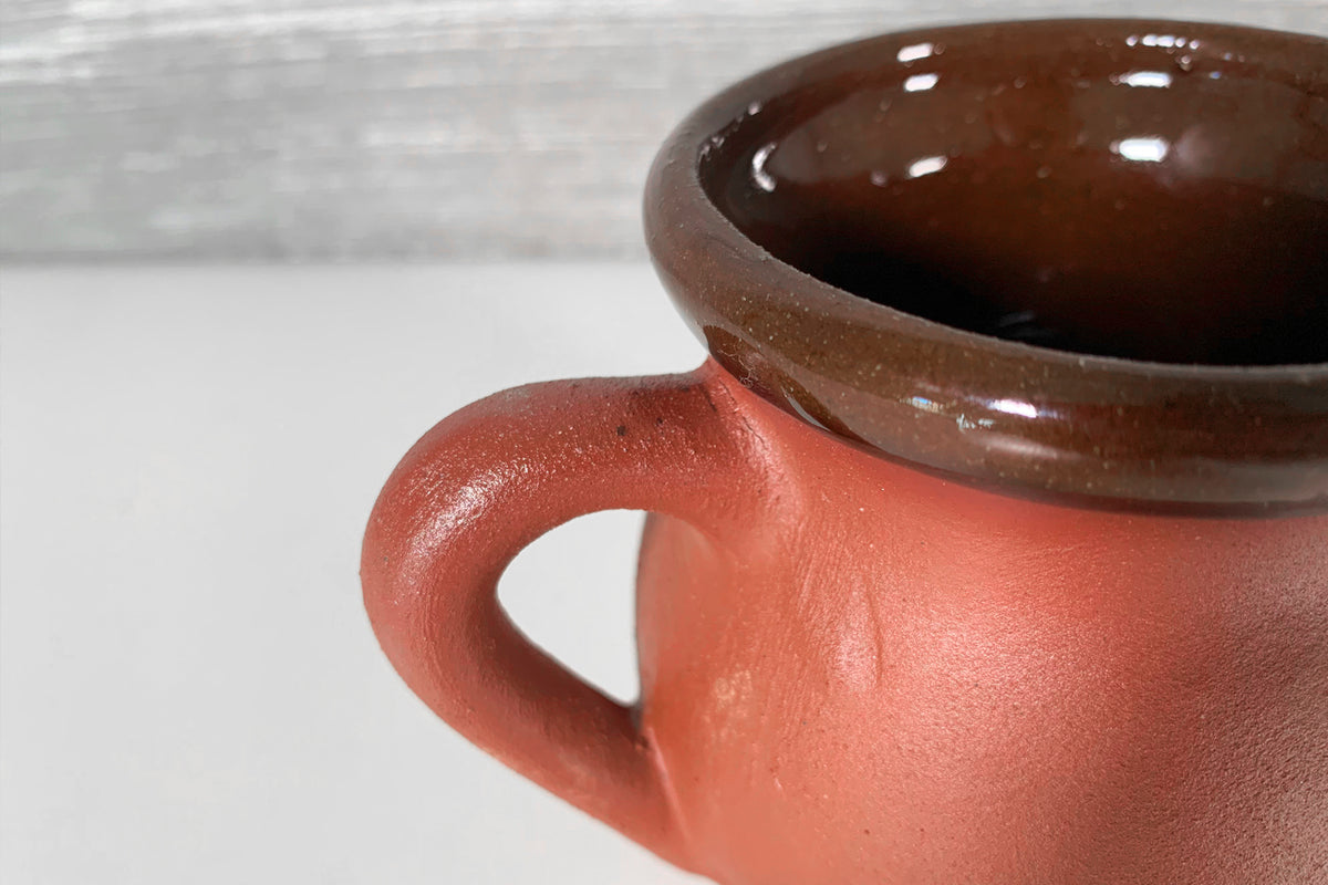 Terracotta mug with brown glaze interior and rounded handle, close-up view.