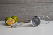 Metal hand juicer with "Verre" engraving and limes, one halved, on white surface.