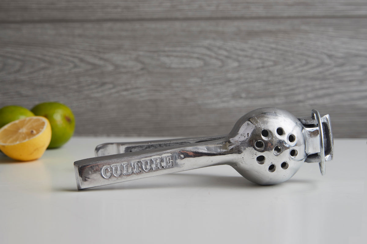 Metal hand juicer with perforated bowl and handles, displayed with cut limes.