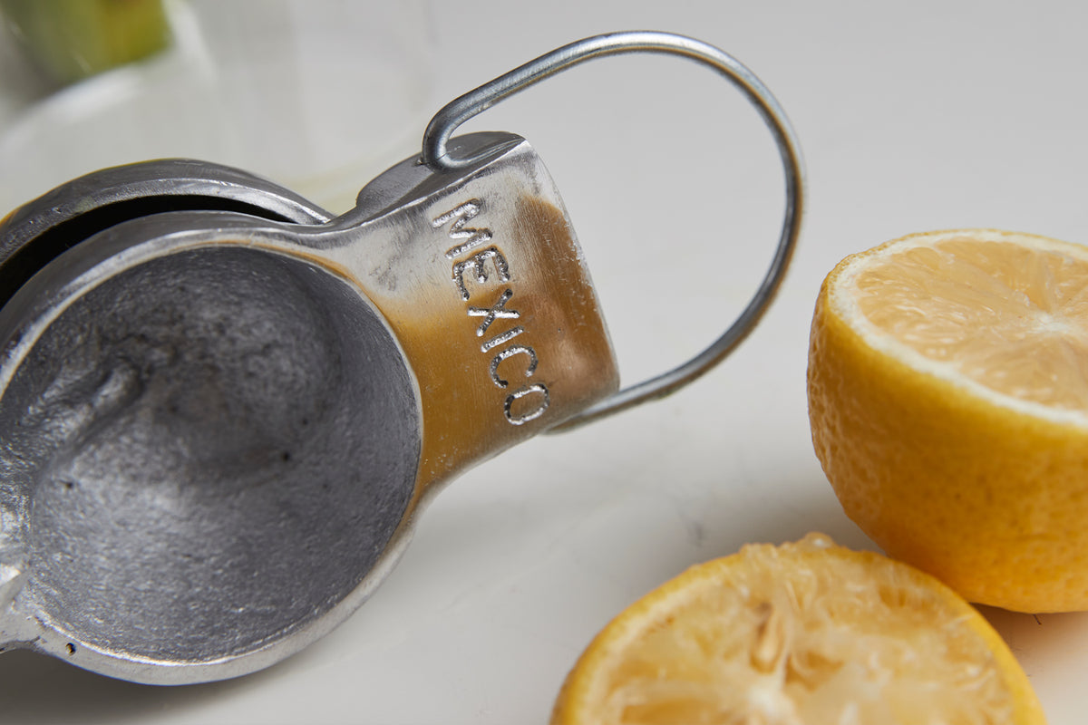 Cast metal hand juicer with handle next to halved lemons on white surface.